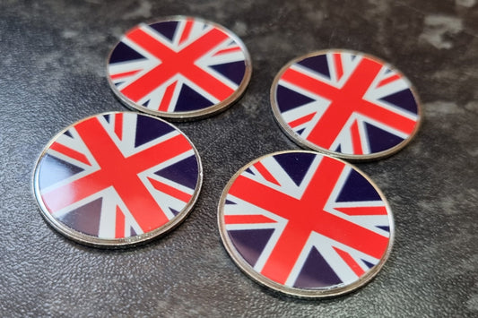 Four round metal golf coin marker featuring the Union Jack flag, arranged on a dark textured surface.